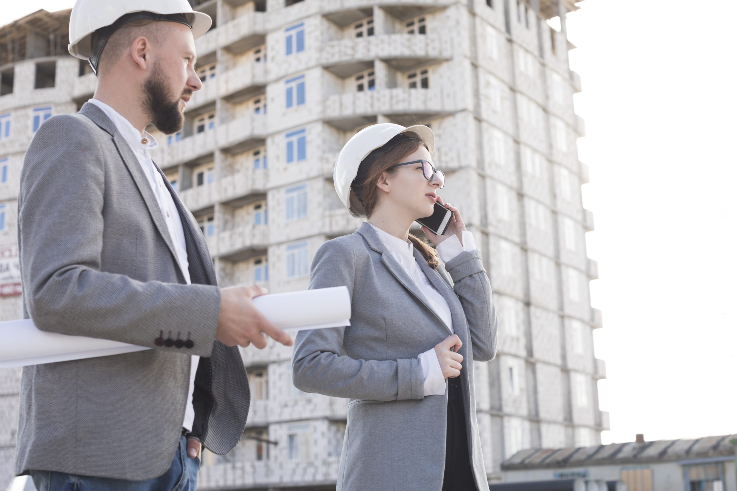 professional-woman-architect-talking-cellphone-standing-with-her-male-colleague-construction-site