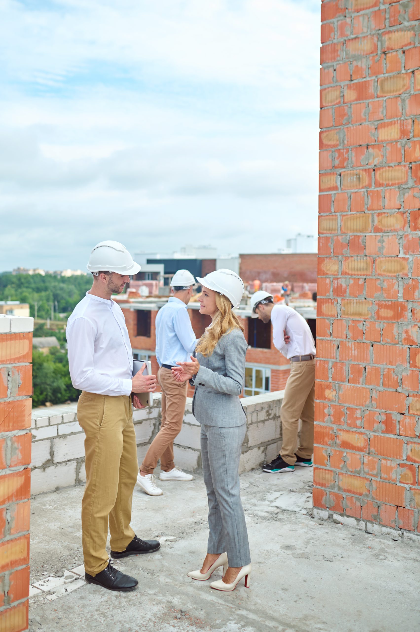 Calm pleased middle-aged stylish construction inspector talking to one of builders on the building site